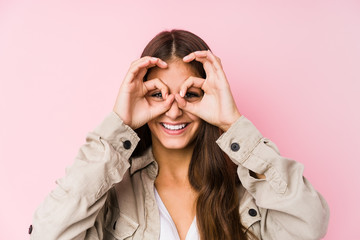 Young caucasian woman posing in a pink background showing okay sign over eyes