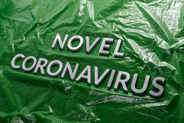 The words novel coronavirus laid with silver metal letters on green crumpled plastic film -...