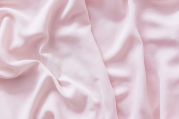 Pink wrinkled silk fabric. The pink fabric is laid out waves. Pink fabric background or texture.