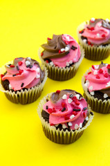 Top View of Pink and White Chocolate Muffins with Heart Candies on Yellow Background