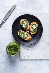 Bruschetta with green arugula pesto and parmesan cheese flakes. Served on black plate. White background