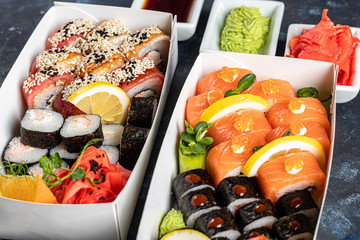 A box of sushi Nigiri, Uramaki California, Philadelphia, on a black stone plate. Sushi menu in a white transport box on a wooden background.
