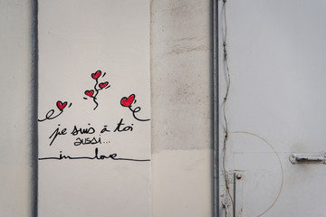 red love hearts graffitti with french writing and heartfelt messages on a tan colored wall in...