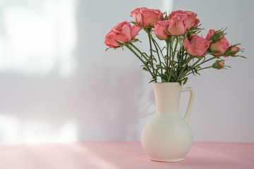 Bouquet of red roses in vase on a pink table on beige background with soft sunlight. Copy space
