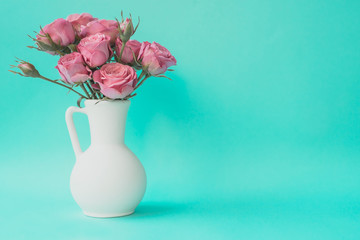 Bouquet of pink roses in white vase on turquoise background. Aqua menthe trendy color. Copy space