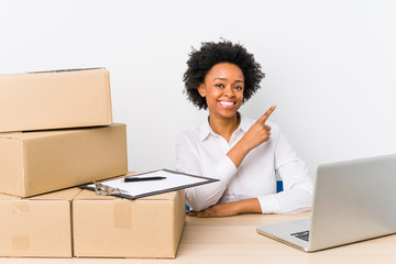 Warehouse manager sitting checking deliveries with laptop smiling and pointing aside, showing...