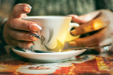 Women's hands with manicured nails holds cup of coffee