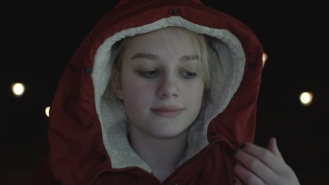 A young girl in a warm jacket puts on a hood in the evening.1920 X 1080 Full Hd.