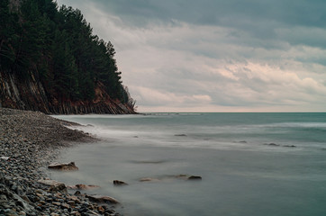  Shot on a long exposure The Black Sea and the stone beach in cloudy weather are located at the foot of pine-covered mountains