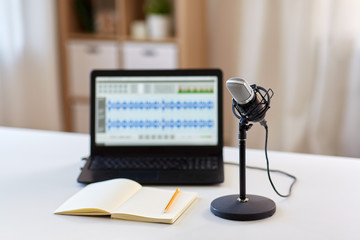 post production and technology concept - microphone, laptop computer with sound editor program, headphones and notebook on table at home office - obrazy, fototapety, plakaty