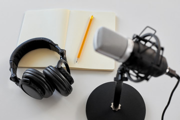 technology, sound recording and podcast concept - headphones , microphone and notebook with pencil...