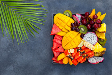 Tropical fruits assortment on a plate. Grey background. Copy space. Top view.