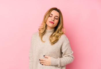 Young blonde cute woman wearing a sweater isolated touches tummy, smiles gently, eating and...