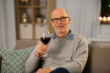 people, alcohol and drinks concept - happy senior man drinking red wine from glass at home in evening