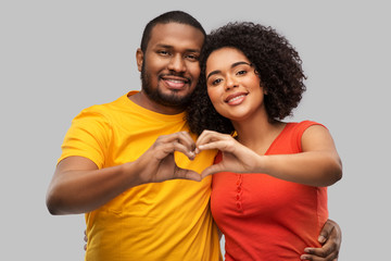 love, valentines day and people concept - happy african american couple making hand heart gesture over grey background