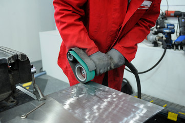 Worker hands sanding metal sheet by the hand held belt sender