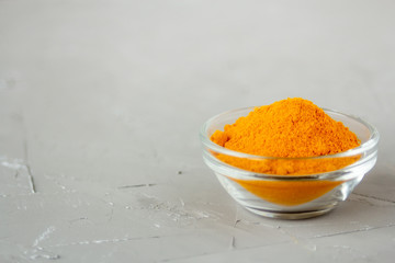 Ground turmeric in a glass plate on a gray background