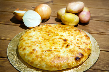 Ossetian pie with potatoes and onions. A traditional dish of ethnic Caucasian cuisine. Dough product with filling on the background of an old wooden table. The concept of tasty and healthy food.