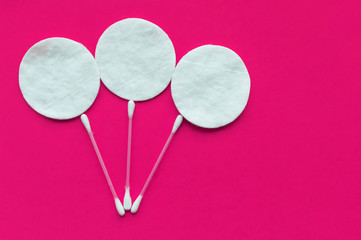 Cotton pads and cotton sticks in the form of balloons on a pink background with a place for writing. The concept of body care.