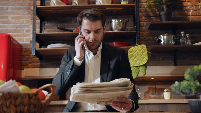 LVIV, UKRAINE - 10 MAY, 2019: Middle aged businessman working from home using laptop, taking some notes, highlighting the information in notebook at kitchen table. Freelancer, workaholic, successful