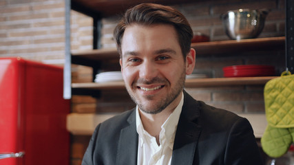 Fototapeta premium Close up young businessman use laptop look at camera smile work in the morning at kitchen computer business home technology work confident male documents internet close up.