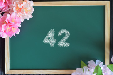 Number 42 write with white chalk, flowers on the board.