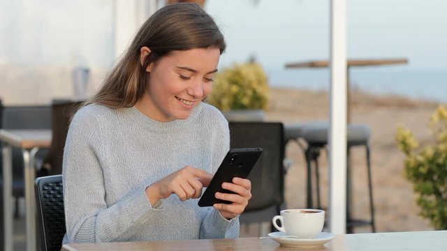 Happy girl using mobile phone sitting in a coffee shop on th ebeach