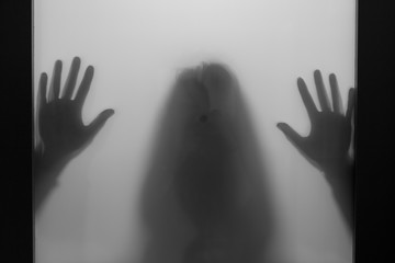 A scary silhouette of a woman's hands and head behind a frosted glass.