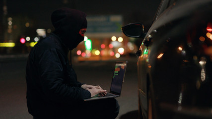 Young robber checking use laptop breaking entering alarm shines a flashlight in a car sitting stealing at night crime male illegal theft stolen danger burglary bandit secure safety insurance door