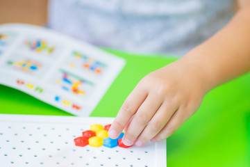 Obraz na płótnie Canvas ?hild collects colorful figurine from a colored plastic mosaic and puzzles on white board. Close up. Preschool development and education of children.