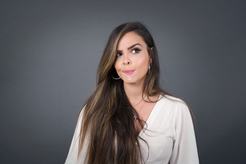 Fototapeta premium Photo of amazed puzzled young Caucasian female with ginger hair knot, curves lips and has worried look, sees something awful in front, isolated on white background, dressed in jean overalls.