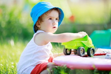 Cute blond curly little boy playing with big green truck