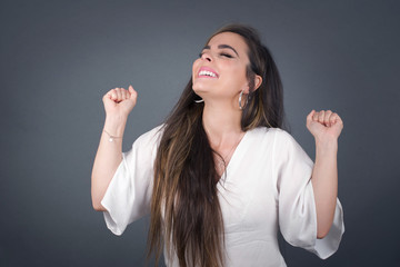 Beautiful young woman happy and excited expressing winning gesture. Successful and celebrating victory, triumphant, gray background.