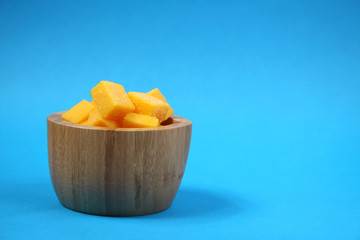 wooden bowl of mango succades isolated on blue background
