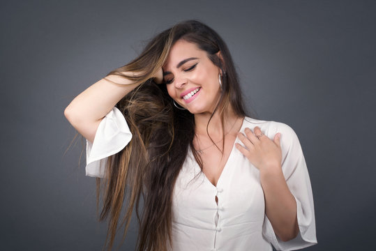 Shot of happy young woman with positive smile, has long hair, rejoices having weekend and good rest after hard working exhausting week, isolated on gray wall. - Powered by Adobe