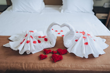 The hotel room is decorated with swans made of white towels with red roses cakes and handmade thread hearts. Photography, concept, composition.