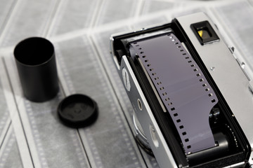 Vintage rangefinder camera on top of a pile of 35mm negatives. Film chamber open with film strip