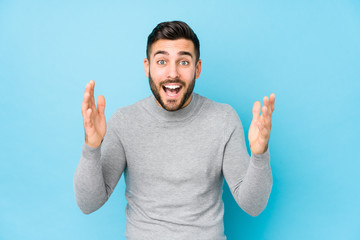 Young caucasian man against a blue background isolated receiving a pleasant surprise, excited and raising hands.