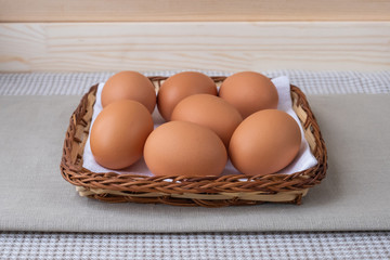 Brown fresh raw eggs lie on a white napkin in a small flat basket. The basket is on the table on a beige background