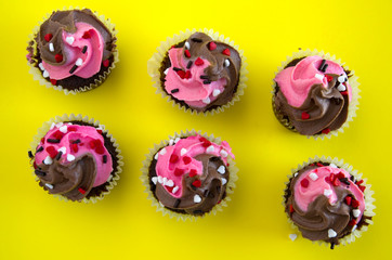 Top View of Pink and White Chocolate Muffins with Heart Candies on Yellow Background