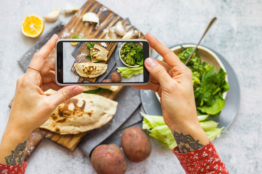 Woman take picture of vegan food with phone at her kitchen. Hand make a closeup smartphone photo of green salad and stuffed bread for blogging or social media content. Vegetarian healthy food.