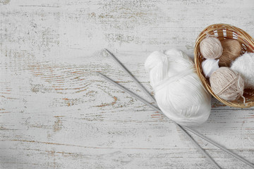 Top view of balls of yarn in pastel colors and knitting needles on a wooden background.