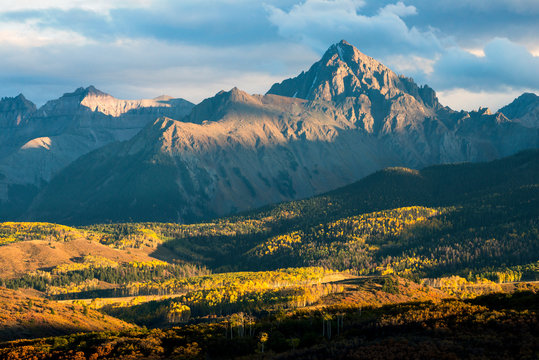 Mears Peak, part of the Sneffels Range, is illuminated in golden light at sunset surrounded by fall color as seen from the Dallas Divide in between the towns of Telluride and Ridgeway, Colorado.