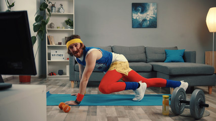 Handsome concentrated sportsman in retro outfit training abs at home. Motivated athlete man trying to get fit exercising on mat and watching sport videos.