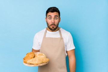Young handsome baker man isolated shrugs shoulders and open eyes confused.