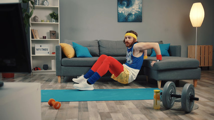 LOS ANGELES, CALIFORNIA, 10 OCTOBER, 2019: Handsome silly sportsman doing exercise leaning on a sofa watching fitness videos at home.