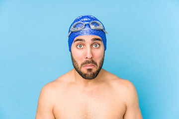 Young handsome swimmer man isolated shrugs shoulders and open eyes confused.