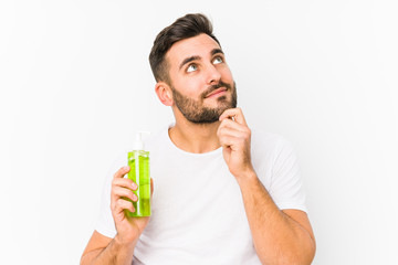 Fototapeta premium Young caucasian man holding a moisturizer with aloe vera isolated looking sideways with doubtful and skeptical expression.