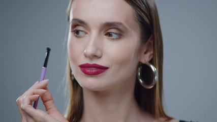 Close up portrait of a young beautiful woman looking directly at the camera and doing a make-up skin attractive beauty fashion brush portrait, caucasian eyes model make up slow motion