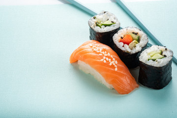 Sushi set with salmon nigiri and roll with cucumber and vegetables with chopsticks on a blue background, for the sushi bar menu